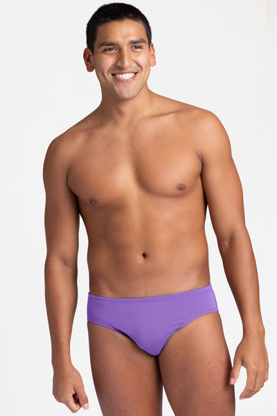 Male model wearing the Men's BROLYN Brief Swimsuit in the Paddle solid, standing in front of a grey background, shown from front view. 
