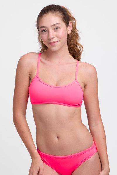 Female model wearing the Women’s Jocelyn Bikini Top in the Hot Pink solid, standing in front of a grey background, shown from front view. 
 