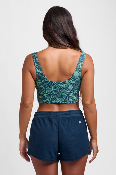 Female model wearing the Women's Eve short in the Trade Winds solid, standing in front of a grey background, shown from the back view. 