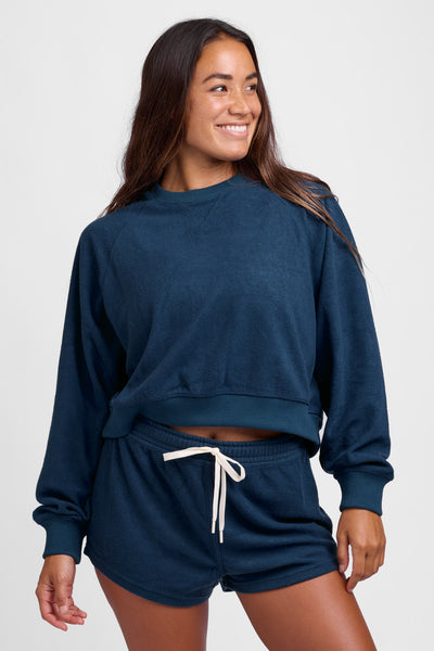 Female model wearing the Women's Eve short in the Trade Winds solid, standing in front of a grey background, shown from the front view. 