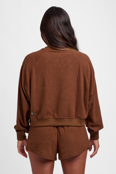 Female model wearing the Women's Maurie Crewneck in the Coconut solid, standing in front of a grey background, shown from the back view. 