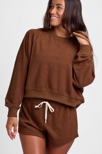 Female model wearing the Women's Maurie Crewneck in the Coconut solid, standing in front of a grey background, shown from the front view. 
