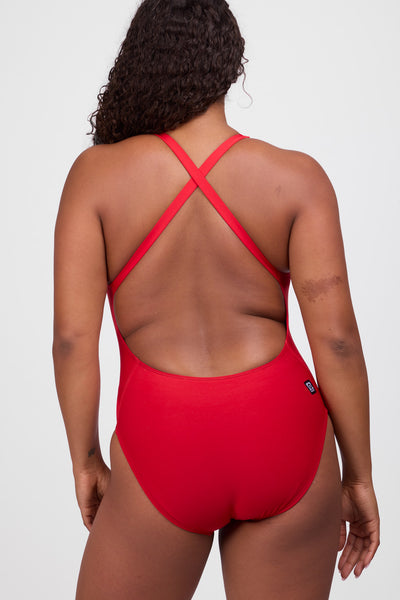 Female model wearing the Women’s Nancy One Piece Swimsuit in the Red solid, standing in front of a grey background, shown from back view. 