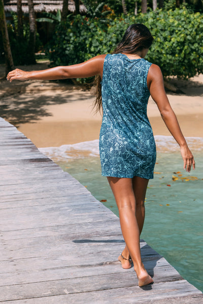 
Female model wearing the Women's Arisa dress in the Sumba printed color, standing in front of the beach, shown from the back view.