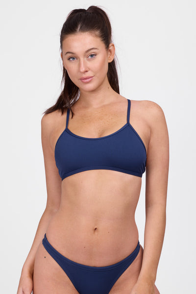 Female model wearing the Women’s Natalie Bikini Top in the Navy solid, standing in front of a grey background, shown from front view. 

