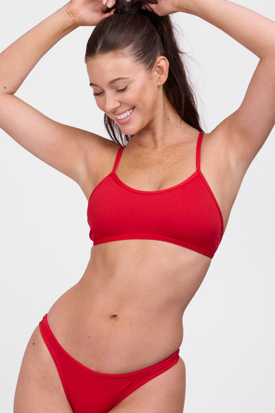 Female model wearing the Women’s Natalie Bikini Top in the Red solid, standing in front of a grey background, shown from front view. 
