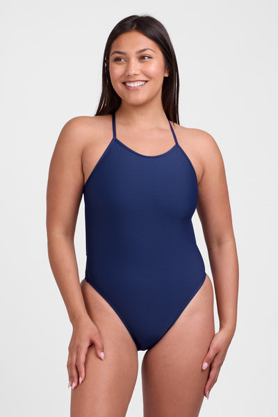 Female model wearing the Women's Brandon One Piece Swimsuit in the Navy solid, standing in front of a grey background, shown from front view. 