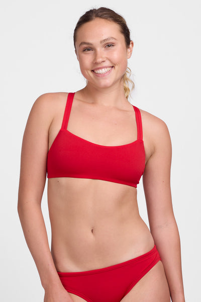 Female model wearing the Women’s Fendrick Bikini Top in the Red solid, standing in front of a grey background, shown from front view. 