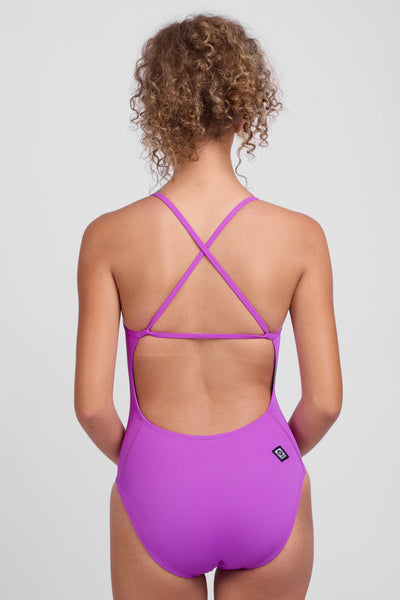 Female model wearing the Women’s Marie One Piece Swimsuit in the Elderberry solid, standing in front of a grey background, shown from back view. 
 