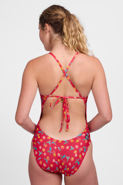 Female model wearing the Women's Jackson One Piece Swimsuit in the Tart print, standing in front of a white background, shown from back view. 