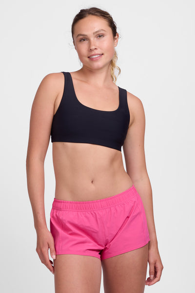 Female model wearing the Women’s Bennie Short in the Cerise solid, standing in front of a grey background, shown from front view. 