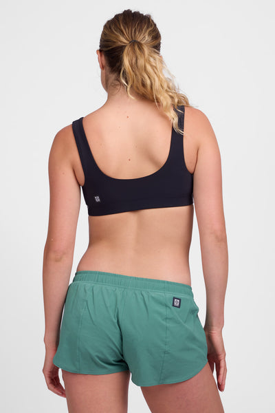 Female model wearing the Women’s Bennie Short in the Fern solid, standing in front of a grey background, shown from back view. 