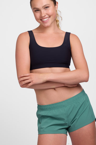 Female model wearing the Women’s Bennie Short in the Fern solid, standing in front of a grey background, shown from front view. 