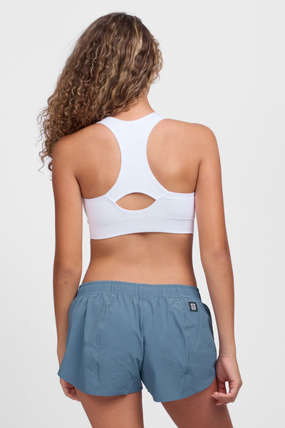 Female model wearing the Women’s Bennie Short in the Midnight Blue solid, standing in front of a grey background, shown from back view. 