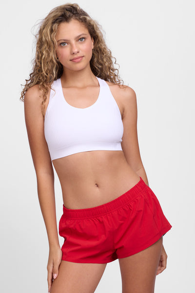 Female model wearing the Women’s Bennie Short in the Red solid, standing in front of a grey background, shown from front view. 