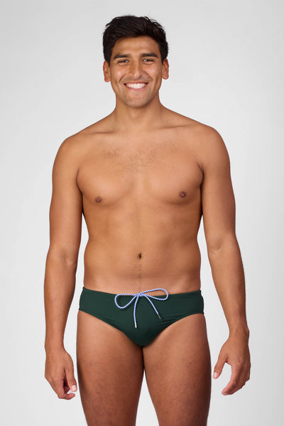 Male model wearing the Men's Brolyn Swim Brief in the Pine solid, standing in front of a grey background shown from the front view