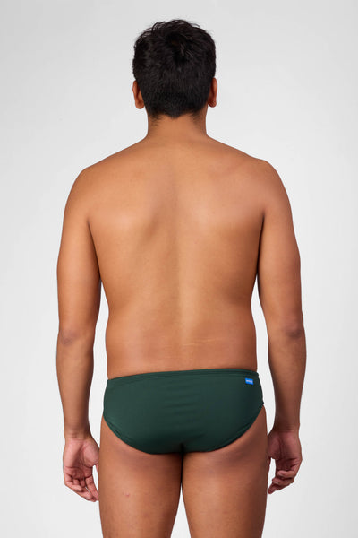 Male model wearing the Men's Brolyn Swim Brief in the Pine solid, standing in front of a grey background shown from the back view