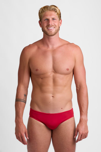 Male model wearing the Men's Brolyn Swim Brief in the Red solid, standing in front of a grey background shown from the front view