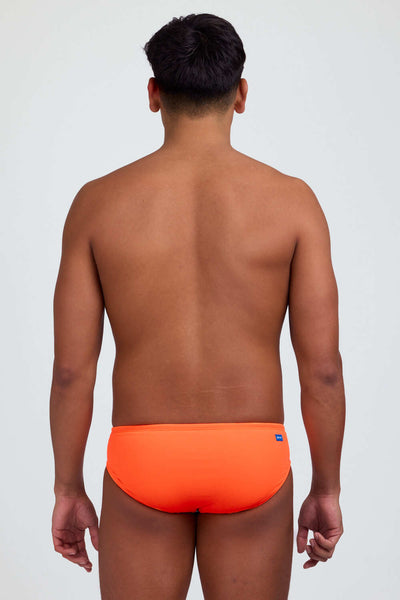
Male model wearing the Men's Brolyn Swim Brief Swimsuit in the Sunkist solid, standing in front of a grey background shown from back view. 