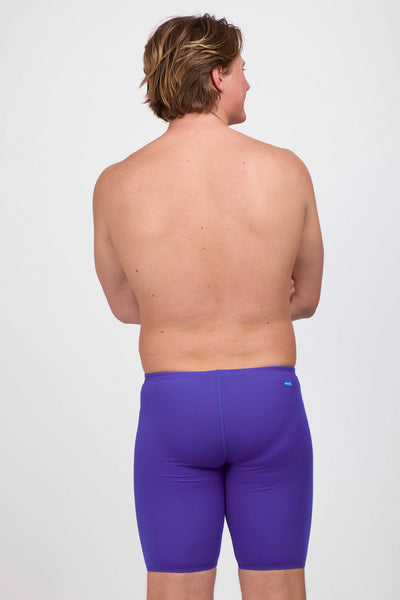 Male model wearing the Men's Brolyn Swim Jammer in the Purple solid, standing in front of a grey background shown from the back view