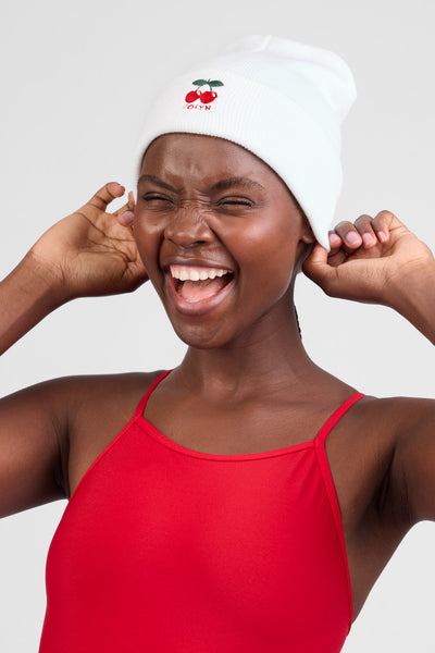 Female model wearing the Unisex beanie in the cherries print, standing in front of a grey background, shown from the front view