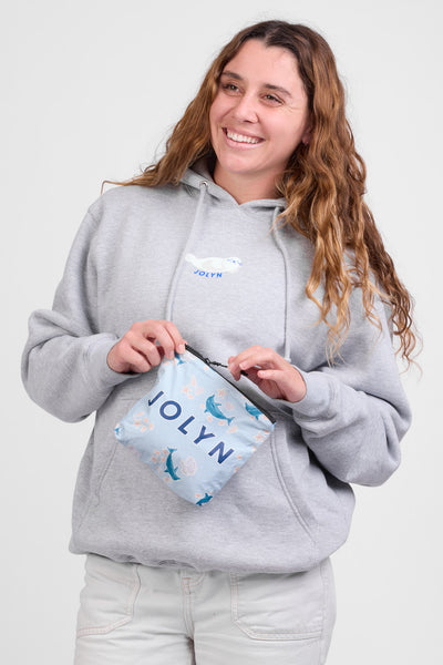 Female model holding a Dry Bag accessory in the Dolphrenz print, standing in front of a grey background, shown from the front view