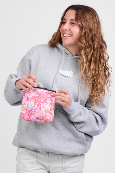 Female model holding up the Dry Bag accessory in the Zinna print,standing in front of a grey background, shown from the front view