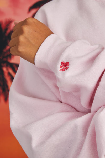 Close up image of the Roxanne Crewneck embroidery flower detail, standing in front of a sunset background, shown from front view