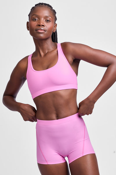 Female model wearing the Women's Anna Tight Short in the Pinky solid, standing in front of a grey background, shown from the front view.