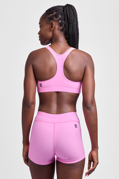 Female model wearing the Women's Anna Tight Short in the Pinky solid, standing in front of a grey background, shown from the back view.