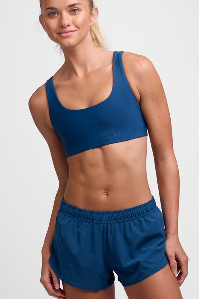 Female model wearing the Women's Lizzie Split Short in the Blue Flame solid, standing in front of a grey background, shown from the front view.