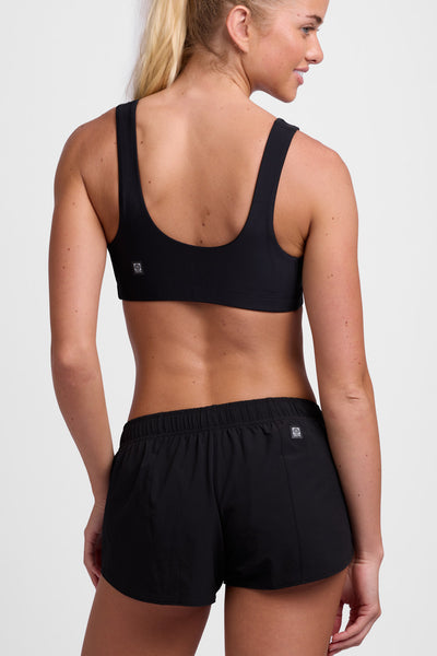 Female model wearing the Women's Rory Short in the Black solid, standing in front of a grey background, shown from the back view.
