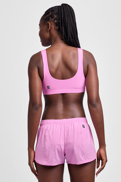 Female model wearing the Women's Rory Short in the Pinky solid, standing in front of a grey background, shown from the back view.