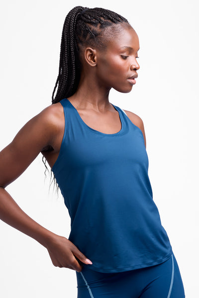 Female model wearing the Women’s Monti Run Singlet in the Blue Flame solid, standing in front of a grey background, shown from front view. 