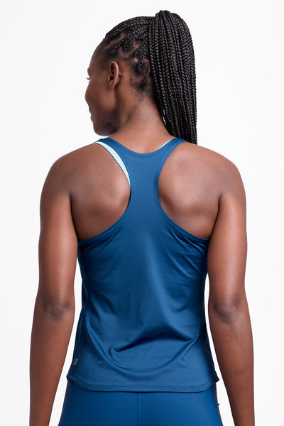 Female model wearing the Women’s Monti Run Singlet in the Blue Flame solid, standing in front of a grey background, shown from back view. 