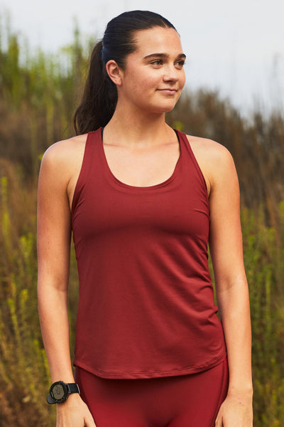Female model wearing the Women’s Monti Run Singlet in the Spice solid, standing in front of a green background, shown from front view. 