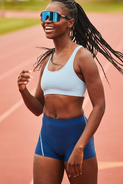 Female model wearing the Women's Molly Sports Bra in the Sky Wave solid, standing in front of a track, shown from the front view.