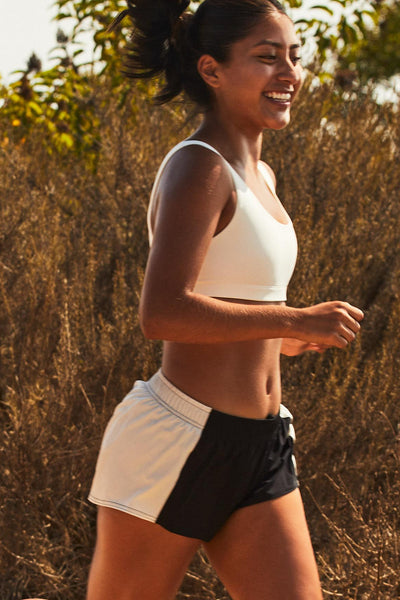 Female model wearing the Women's Rory Short in the Black contrast, standing in front of a green background, shown from the side view.