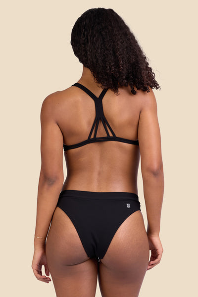 Female model wearing the Women's Alanna Bikini Bottom in the Black Ribbed solid, standing in front of a yellow background shown from the back view

|| Size S, Hips 37"