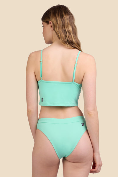 Female model wearing the Women's Alanna Bikini Bottom in the Mint Tulip solid, standing in front of a yellow background shown from the back view

|| Size S, Hips 37"  
