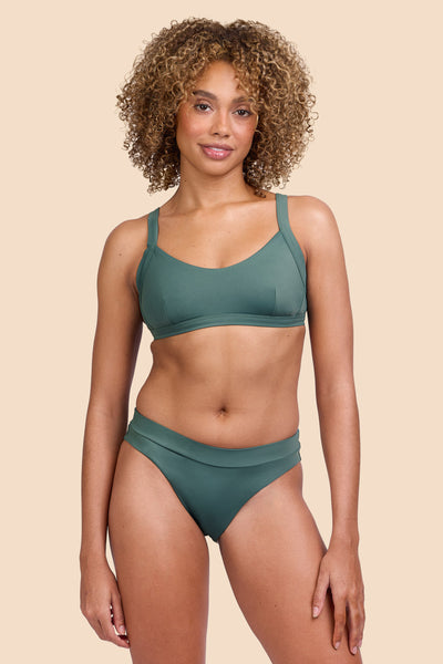 Female model wearing the Womens Alanna Bikini Bottom in the Zucchini solid, standing in front of a yellow background shown from the front view

|| Size S, Hip 36"  