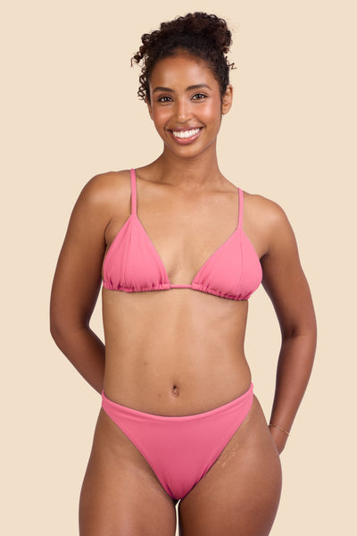 Female model wearing the Women's Ava Bikini Bottom in the Tea Rose Ribbed solid, standing in front of a yellow background shown from the front view

|| Size S, Hips 37"  
