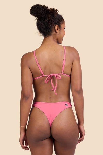 Female model wearing the Women's Ava Bikini Bottom in the Tea Rose Ribbed solid, standing in front of a yellow background shown from the back view

|| Size S, Hips 37"  
