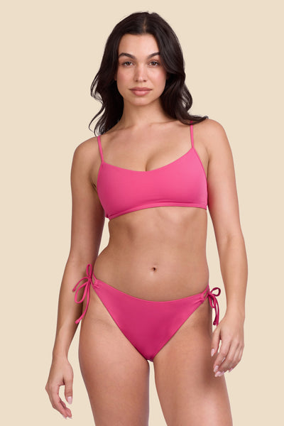 Female model wearing the Women's Bella Bikini Bottom in the Berry solid, standing in front of a yellow background shown from the front view

|| Size S, Hips 34"  
