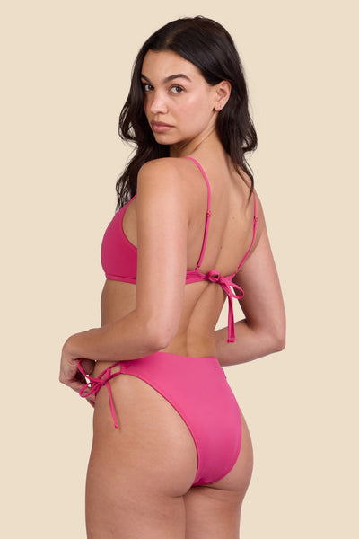 Female model wearing the Women's Bella Bikini Bottom in the Berry solid, standing in front of a yellow background shown from the side view

|| Size S, Hips 34"  
