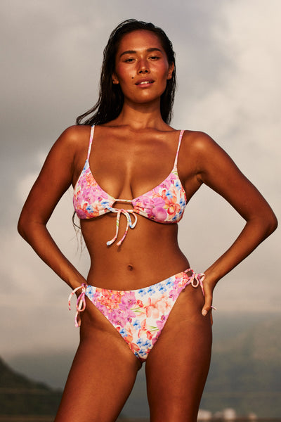 Female model wearing the Women's Bella Bikini Bottom in the Orchids ribbed print, standing in front of a beach shown from the front view