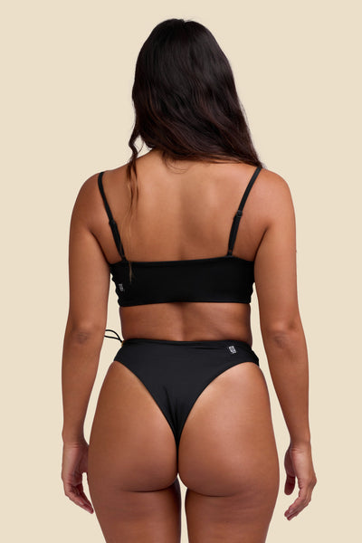 Female model wearing the Women's Ciara Bikini Bottom in the Black solid, standing in front of a yellow background shown from the back view

|| Size S, Hips 35"  