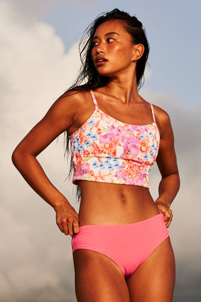 Female model wearing the Women's Dakota Bikini Bottom in the Tea Rose Ribbed solid, standing in front of a beach shown from the front view