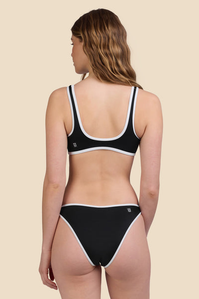 Female model wearing the Women's Dina Bikini Bottom in the Black solid, standing in front of a yellow background shown from the back view

|| Size S, Hips 37"  