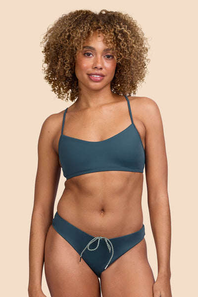 Female model wearing the Women's Gina Bikini Bottom in the Underwater solid, standing in front of a yellow background shown from the front view

|| Size S, Hip 36"  